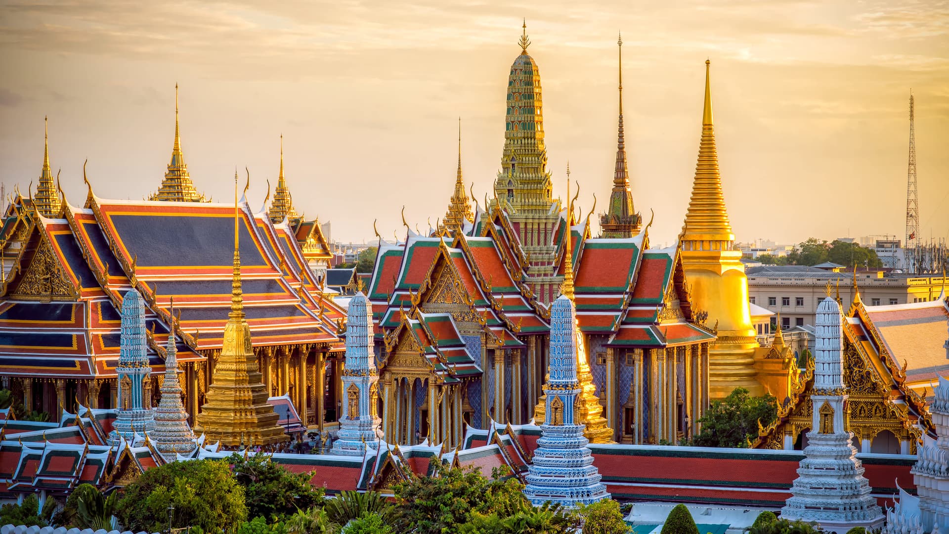 Stunning panorama of Bangkok's Grand Palace at sunset with golden spires and ornate temple rooftops